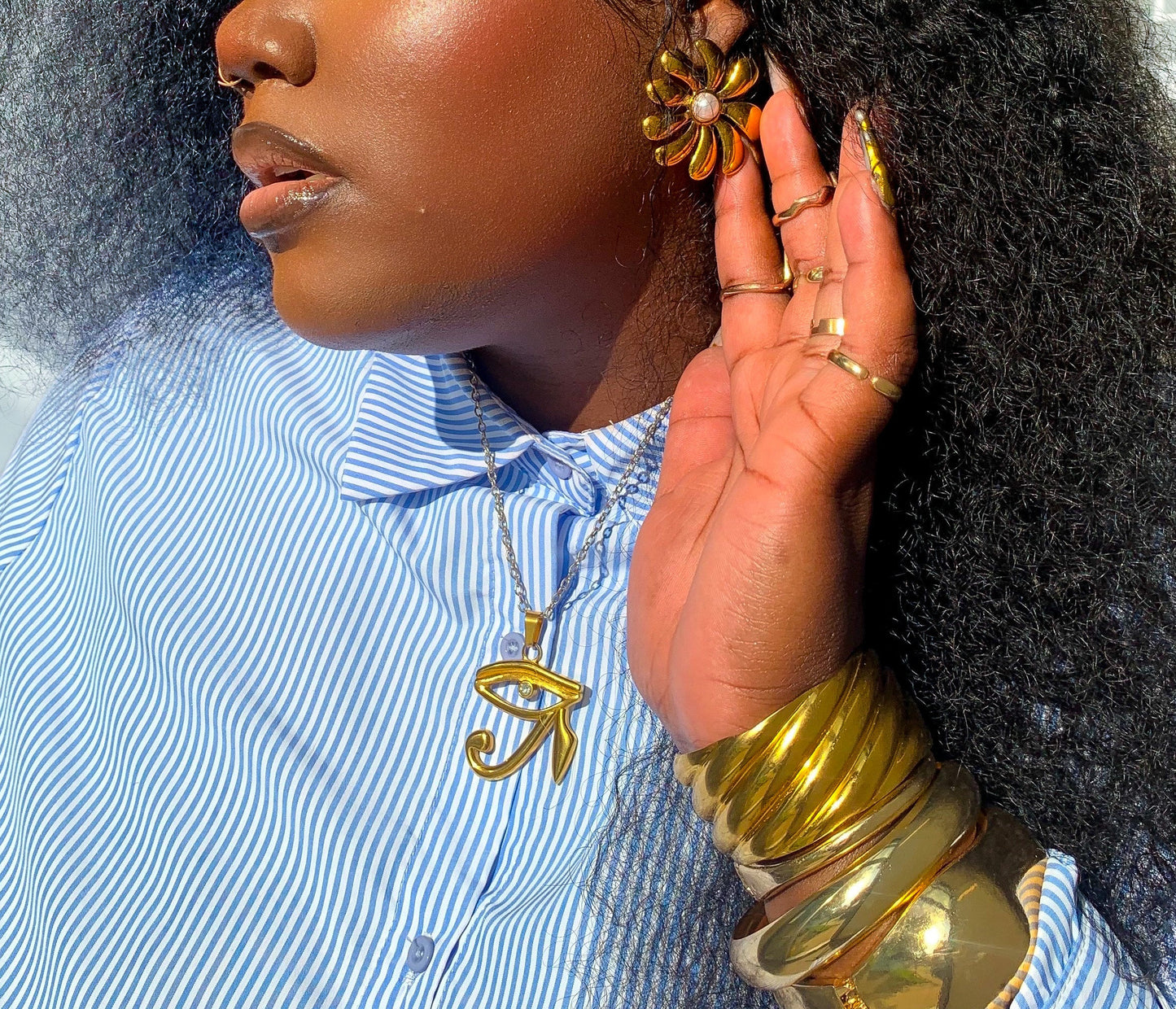 Woman wearing gold jewelry including earrings and bracelets, with a blurred background