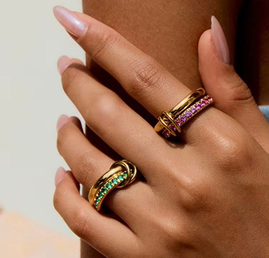 Hand wearing two gold rings with gemstones on a neutral background