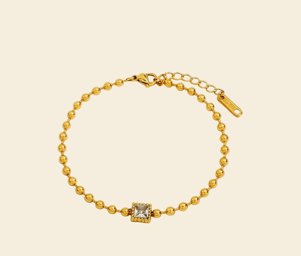 Gold bracelet with a square pendant on a white background