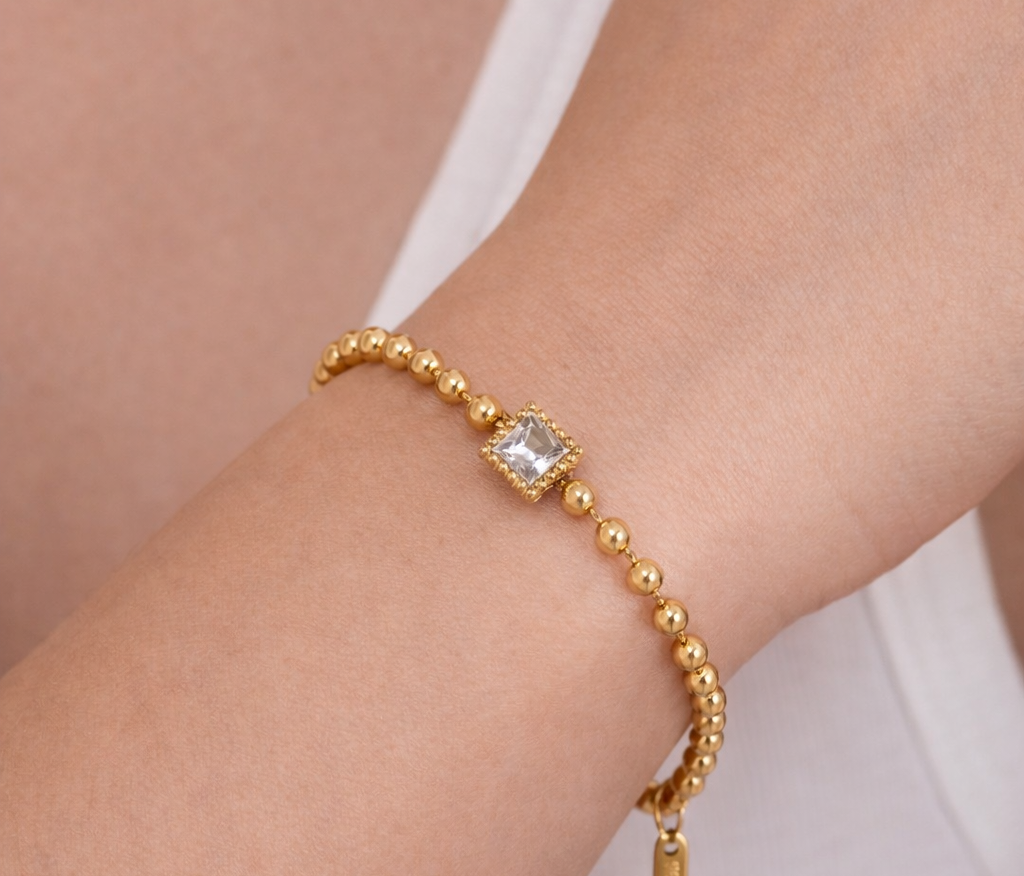 Gold bracelet with a clear gemstone on a wrist against a neutral background