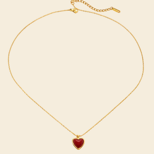 Gold necklace with a red heart pendant on a white background