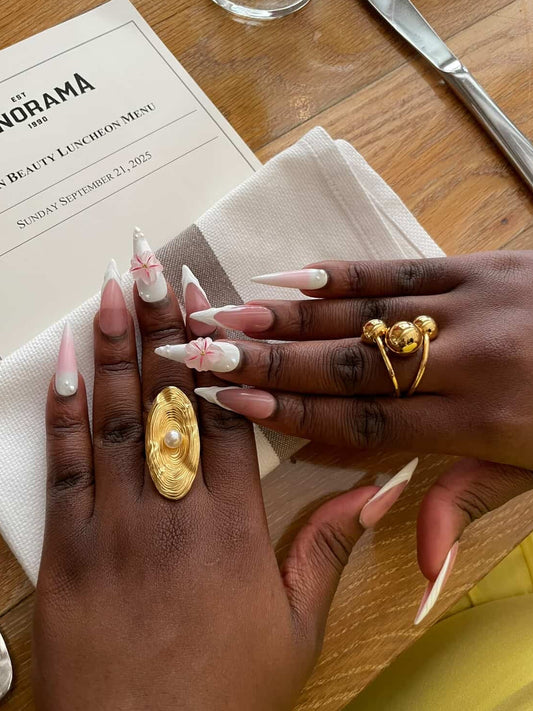 Close-up of hands with gold rings and nail art on a wooden table.