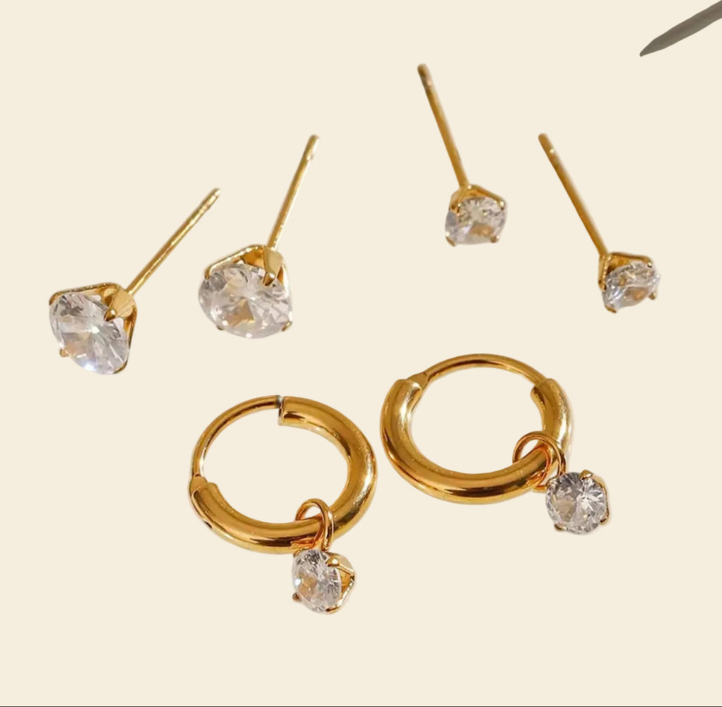 Gold earrings with clear gemstones on a beige background