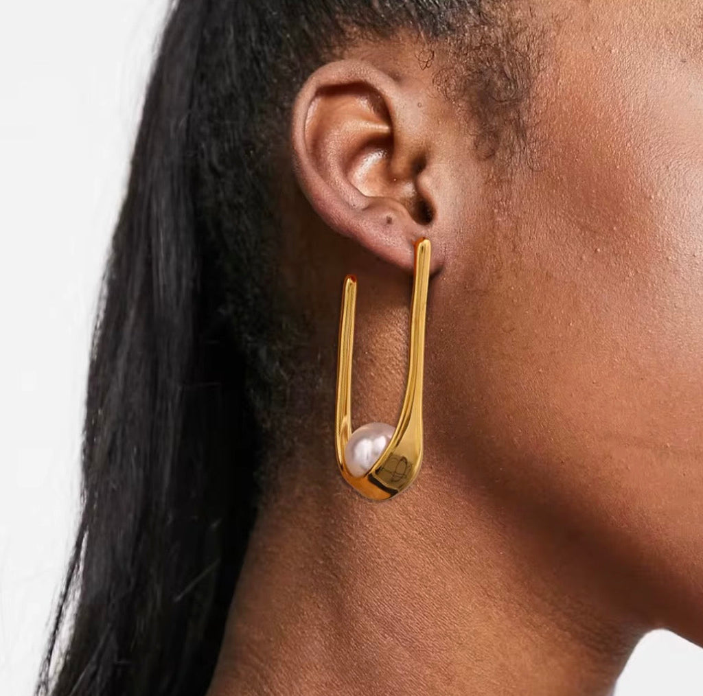 Gold earring with a pearl on a person's ear against a neutral background
