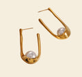 Gold earrings with pearl-like stones on a stone surface