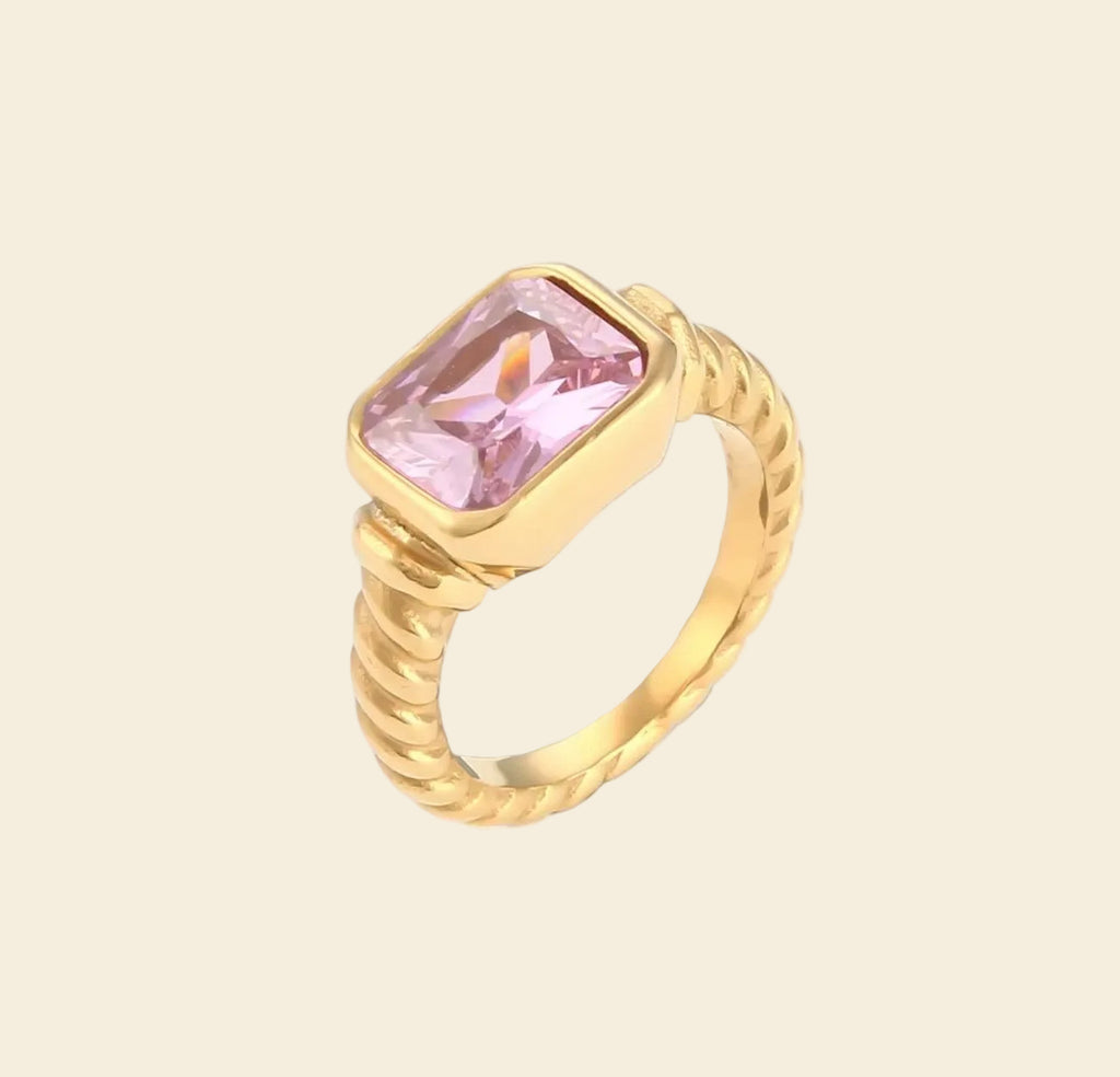 Gold ring with a pink gemstone on a beige background