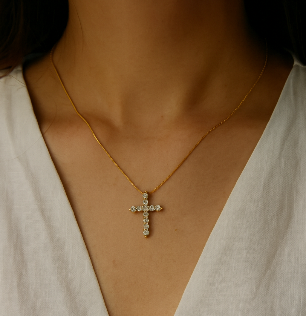 Gold necklace with a cross pendant worn by a person in a white top.